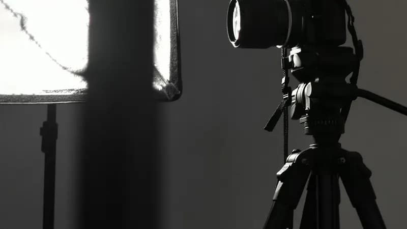 Un appareil photo monté sur trépied, face à une boîte à lumière, dans un studio.