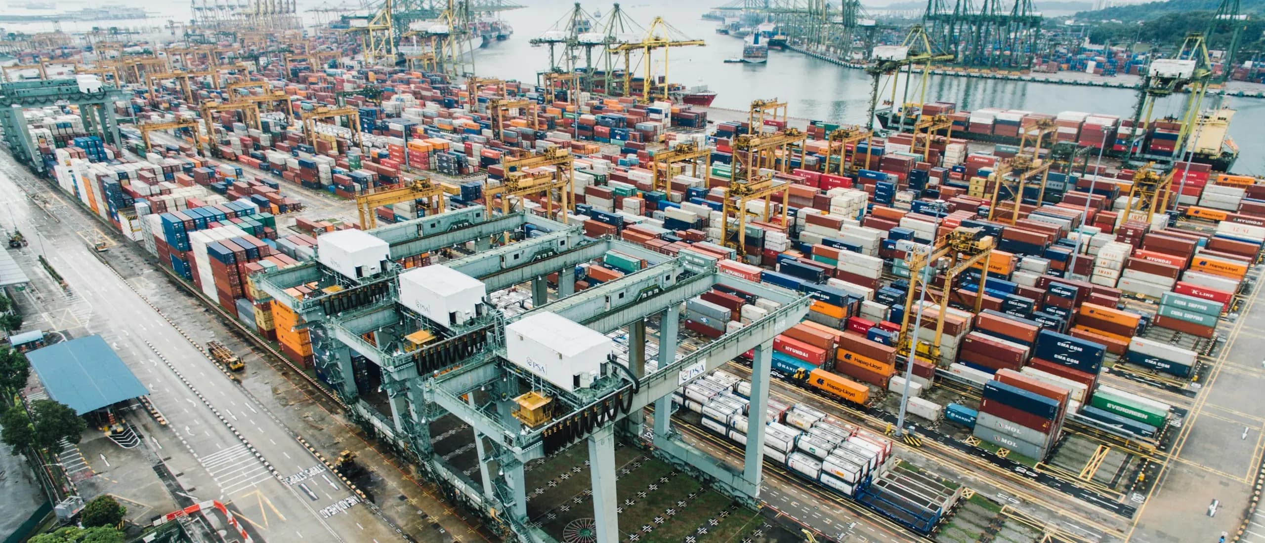 Un terminal portuaire vu du ciel : conteneurs empilés par centaines, portiques et navires à quai.