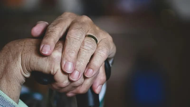 Les mains d’une personne âgée, posées l’une sur l’autre sur le pommeau d’une canne.