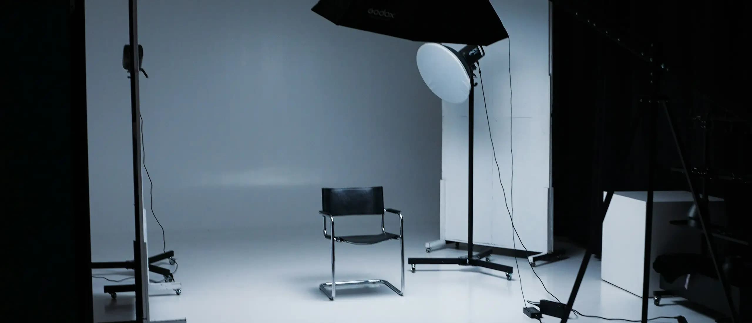 Un studio photo vide : une boîte à lumière sur pied éclaire un fond blanc et une chaise.