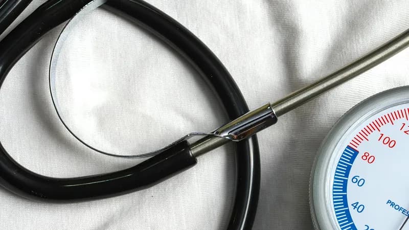 Un stéthoscope posé sur un drap blanc, à côté du cadran gradué d’un tensiomètre.